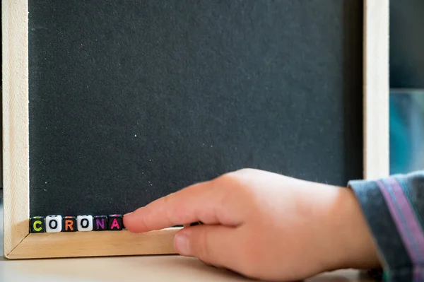 Gyermek írás CORONA segítségével ábécé gyöngyök fekete táblán. — Stock Fotó