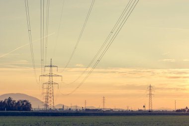 Gün batımında tarlalarda çalışan güç iletim hatları.