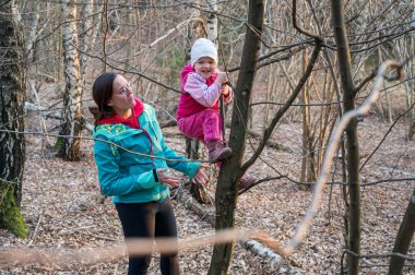 Gururlu aktif anne, kızının ormanda ağaca tırmanmasına yardım ediyor..