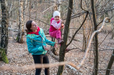 Gururlu aktif anne, kızının ormanda ağaca tırmanmasına yardım ediyor..