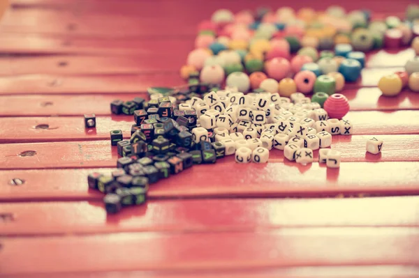 Many alphabet beads scattered on red table ready to play.