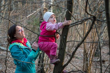 Gururlu aktif anne, kızının ormanda ağaca tırmanmasına yardım ediyor..