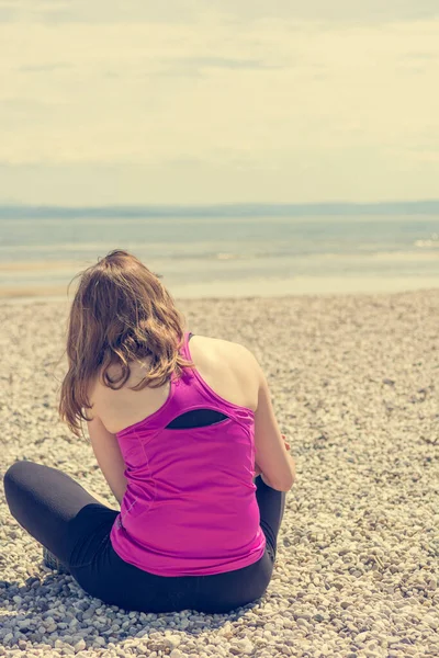 Active woman applying sunscreen spray on a pebble beach.