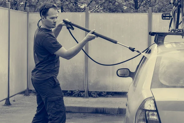 Mladý muž čištění jeho auto pomocí tryskové myčky na samoobslužné stanici. — Stock fotografie