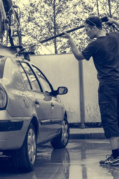 Giovane uomo che pulisce la sua auto utilizzando jet washer alla stazione di self service . — Foto Stock