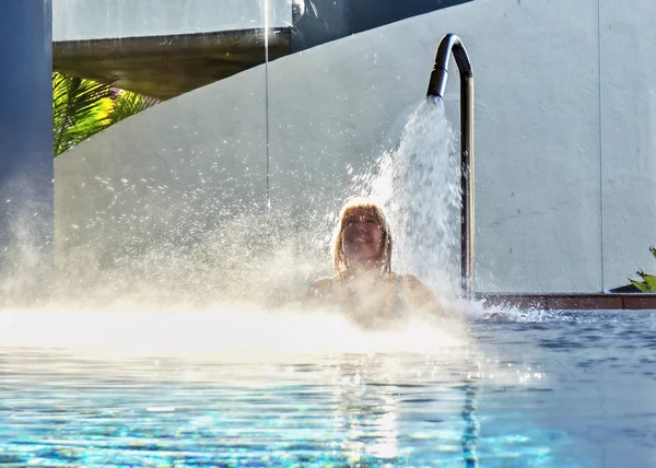 A blonde woman is standing under a strong jet of water