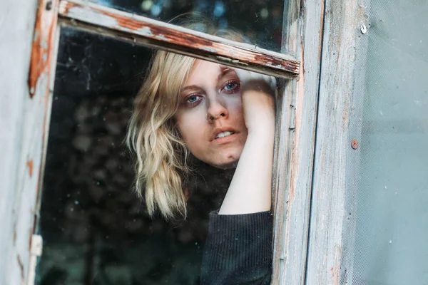Блондинка с голубыми глазами, смотрящая в старое окно . — стоковое фото