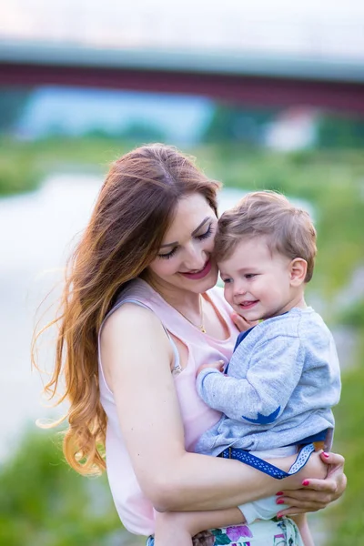 Jovem mãe segurando seu lindo filho loiro, olhando para ele com amor — Fotografia de Stock