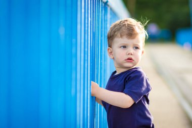 Mavi tişörtlü şirin çocuk ayakta duruyor, kafası karışmış görünüyor. Evrensel Çocuk Günü