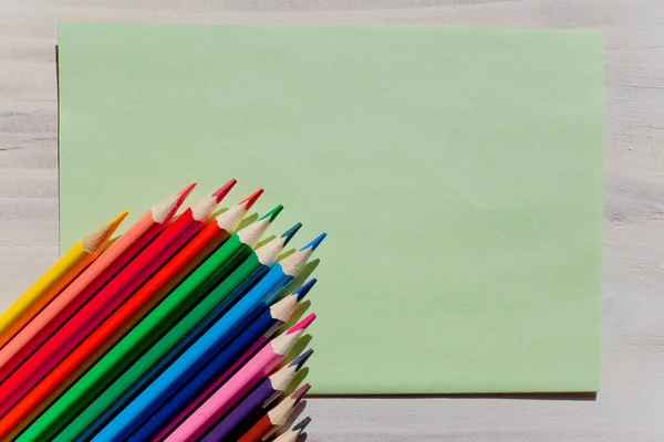 Multicolored wooden pens with empty piece of paper. Background, texture, patters