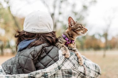 Sahibi omzunda sevimli, genç, çizgili bir evcil kedi taşıyor..
