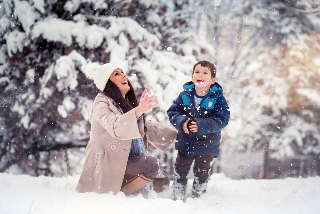 Beautiful, young mom and her cute son enjoying winter, playing with snow