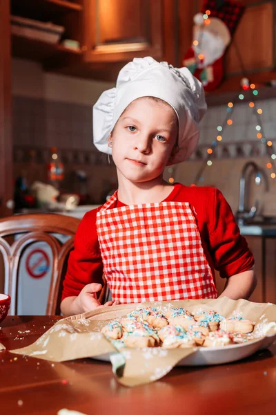앞치마와 모자를 쓰고 생강 쿠키를 제공하는 셰프 유니폼을 입은 귀엽고 작은 소녀. — 스톡 사진