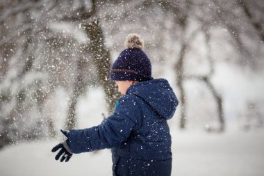 Sevimli, sevimli çocuk neşeyle karla oynuyor. Kış zamanı, çocuk aktiviteleri.