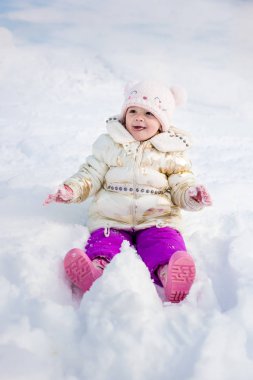 Beyaz ceketli küçük kız eğleniyor, dışarıda oynuyor, karla çevrili.