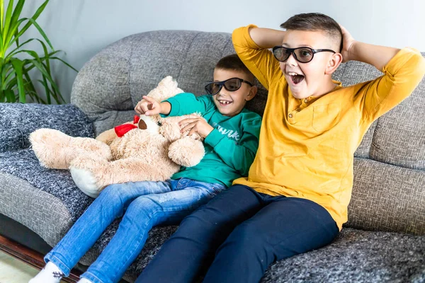 Cute boys watching scary movie with 3d glasses, together with teddy bear toy