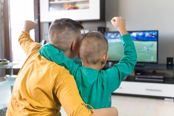 Діти дивляться футбол по телевізору, вітають, тримають руки в повітрі — стокове фото