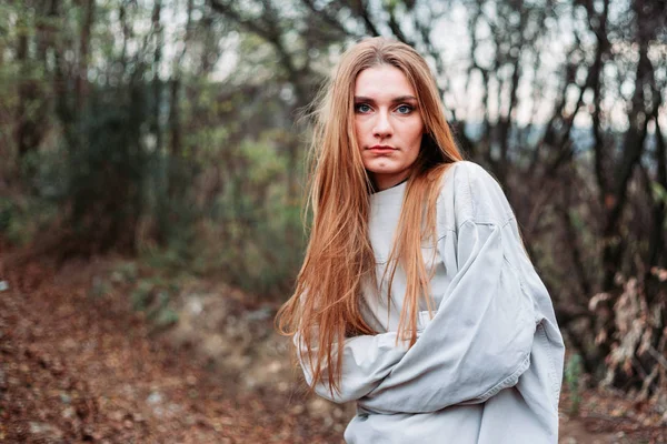 Девушка с длинными волосами в смирительной рубашке, в лесу, выглядит испуганной. . — стоковое фото
