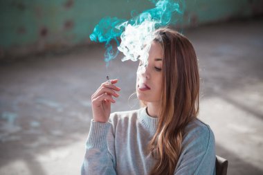 Gri kazaklı asi kız sigara içiyor. Sağlıksız alışkanlıklar, sigarayı bırak.