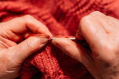 Yaşlı kadın elleri, kırmızı süveter örüyor. Hobi ve eğlence.
