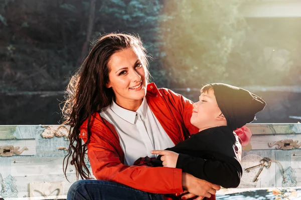 彼女の息子を抱いている若い母親は、彼は彼女の膝の上に横たわっている。屋外の写真 — ストック写真