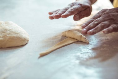 Kadın eli hamuru rulo şeklinde yuvarlıyor. Kruvasan rulosu yapma süreci