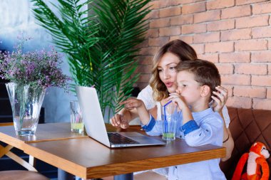 Anne ve oğlu masada dizüstü bilgisayara bakıyor. Ebeveynlik ve teknoloji