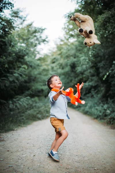 Netter kleiner Junge, der mit seinen Spielzeugfreunden in der Natur spielt. Erziehung gesunder Kinder — Stockfoto