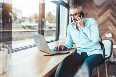 Ofis penceresinin yanında konuşan mavi gömlekli orta yaşlı bir adam..