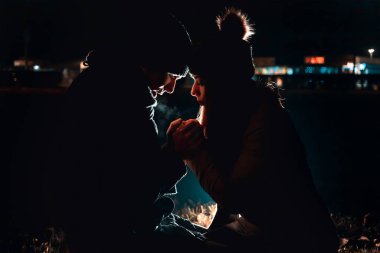 Young couple holding hands, warming them. Nighttime. cold weather. Bokeh lights