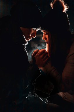 Young couple holding hands, warming them. Nighttime. cold weather. Bokeh lights