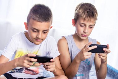 Çocuklar, kardeşler akıllı telefonlarıyla oyun oynuyorlar. İnternet bağımlılığı