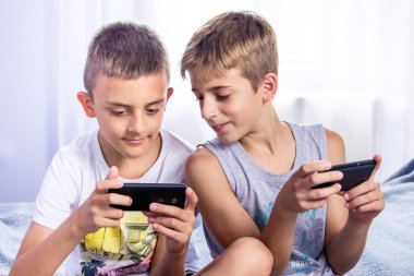 Çocuklar, kardeşler akıllı telefonlarıyla online oyun oynuyorlar. Modern çocuk etkinliği
