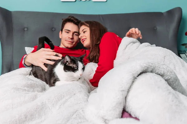 Couple lying in bed with their cute black and white cat. People and pets — Stockfoto