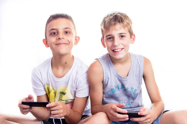 Милі хлопчики, брати грають в онлайн ігри на своїх смартфонах . — стокове фото