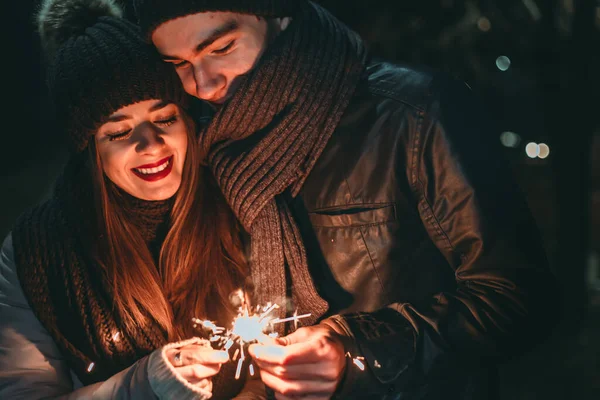 Linda pareja joven con ropa de invierno sosteniendo bengalas. Día de San Valentín —  Fotos de Stock