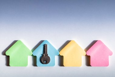 Mavi arka planda metal anahtarı olan boş renkli ev çerçeveleri. Ev satın alınıyor