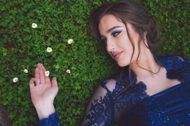 Beautiful girl in glamorous ultramarine dress lying on the grass.
