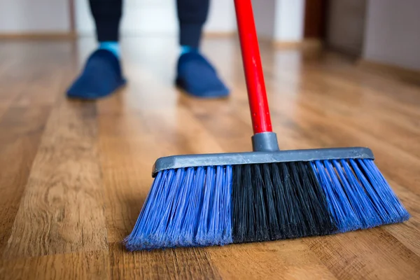 Esposa en zapatillas azules usando escoba azul interior para la limpieza de pisos de madera . — Foto de Stock