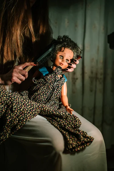 Chica de traje de noche peinando el pelo de muñecas viejas. Concepto extraño y perturbador — Foto de Stock