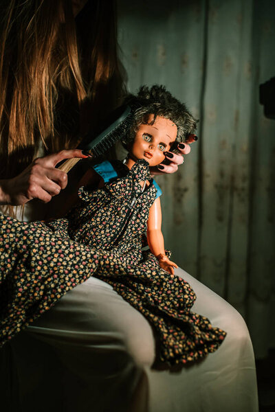 Girl in night gown combing old dolls hair. Bizarre, disturbing concept