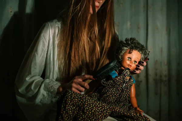 Gadis berpakaian malam menyisir rambut boneka tua. Luar biasa, konsep yang mengganggu — Stok Foto