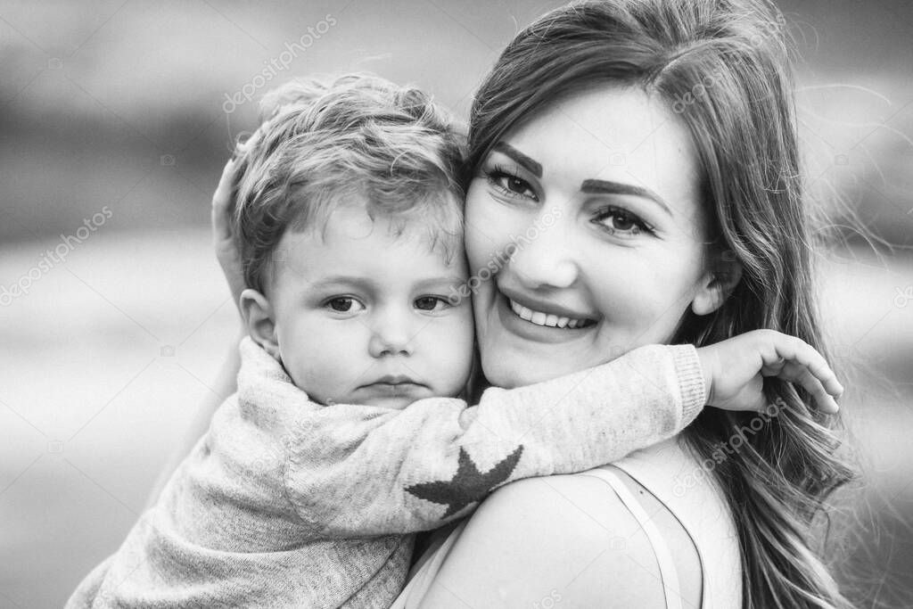 Young mom holding her beautiful blond son. Parents and children relationship.  Black and white photo. Mothers day