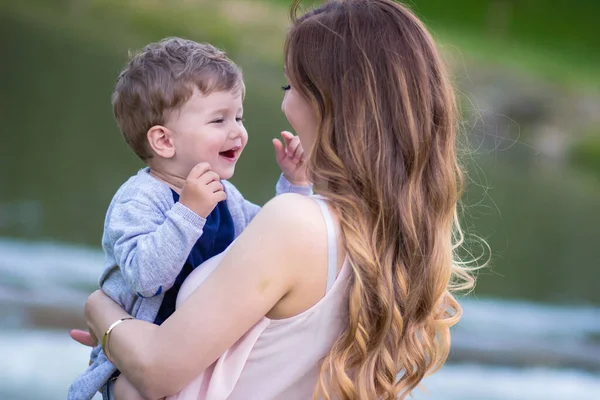 Jovem Mãe Segurando Seu Lindo Filho Loiro Olhando Para Ele — Fotografia de Stock