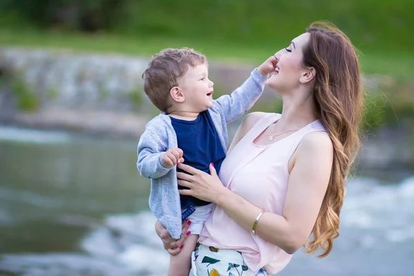 Jovem Mãe Segurando Seu Lindo Filho Loiro Olhando Para Ele — Fotografia de Stock