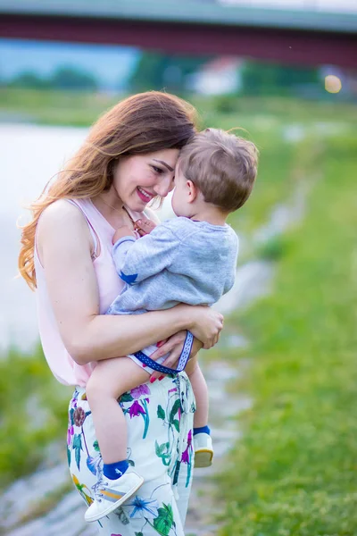 Jovem Mãe Segurando Seu Lindo Filho Loiro Olhando Para Ele — Fotografia de Stock