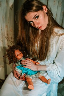 Gecelikli bir kız ellerinde oyuncak bebekleri tutuyor. Tuhaf, rahatsız edici bir kavram.
