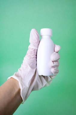 Ellerinde plastik şişe tutan bir eldiven. Mesaj için yer var. Yeşil arka plan. Corona virüsü konsepti