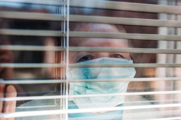 Фото Пожилой Женщины Медицинской Хирургической Маской Лице Смотрящей Окно Изнутри — стоковое фото