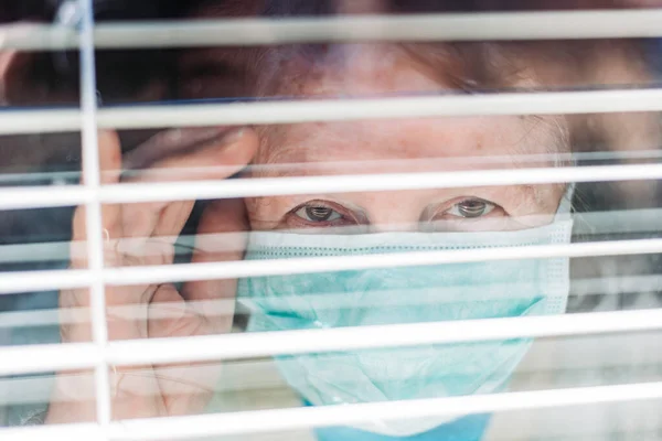 Фото Пожилой Женщины Медицинской Хирургической Маской Лице Заглядывающей Окно Изнутри — стоковое фото